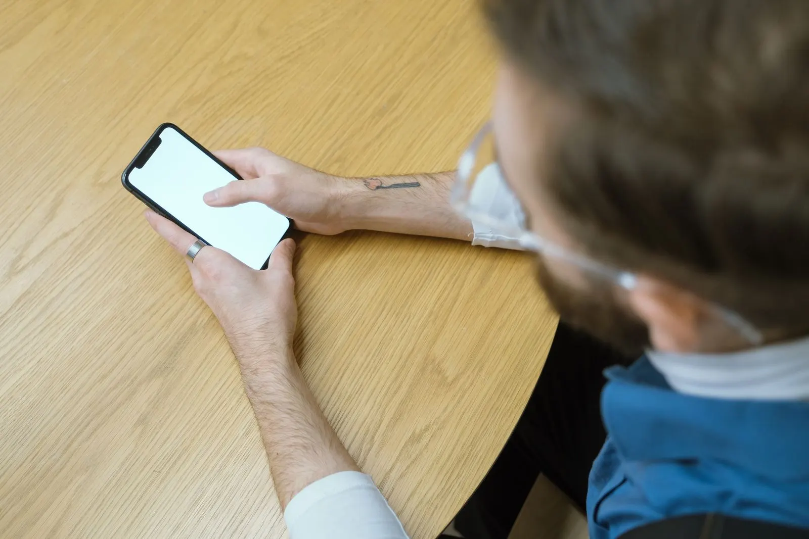 Hände halten ein Smartphone über einem Holztisch