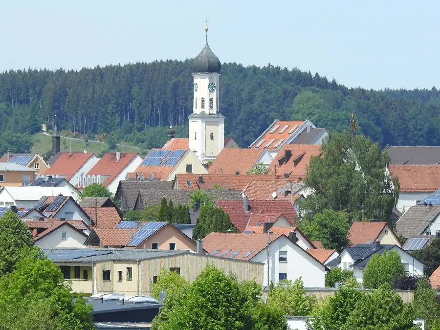 Ortsansicht von Zusmarshausen mit Kirchturm vor bewaldetem Hang